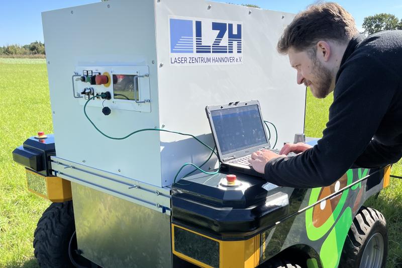 Wissenschaftler arbeitet mit Laptop an einem Feldroboter.