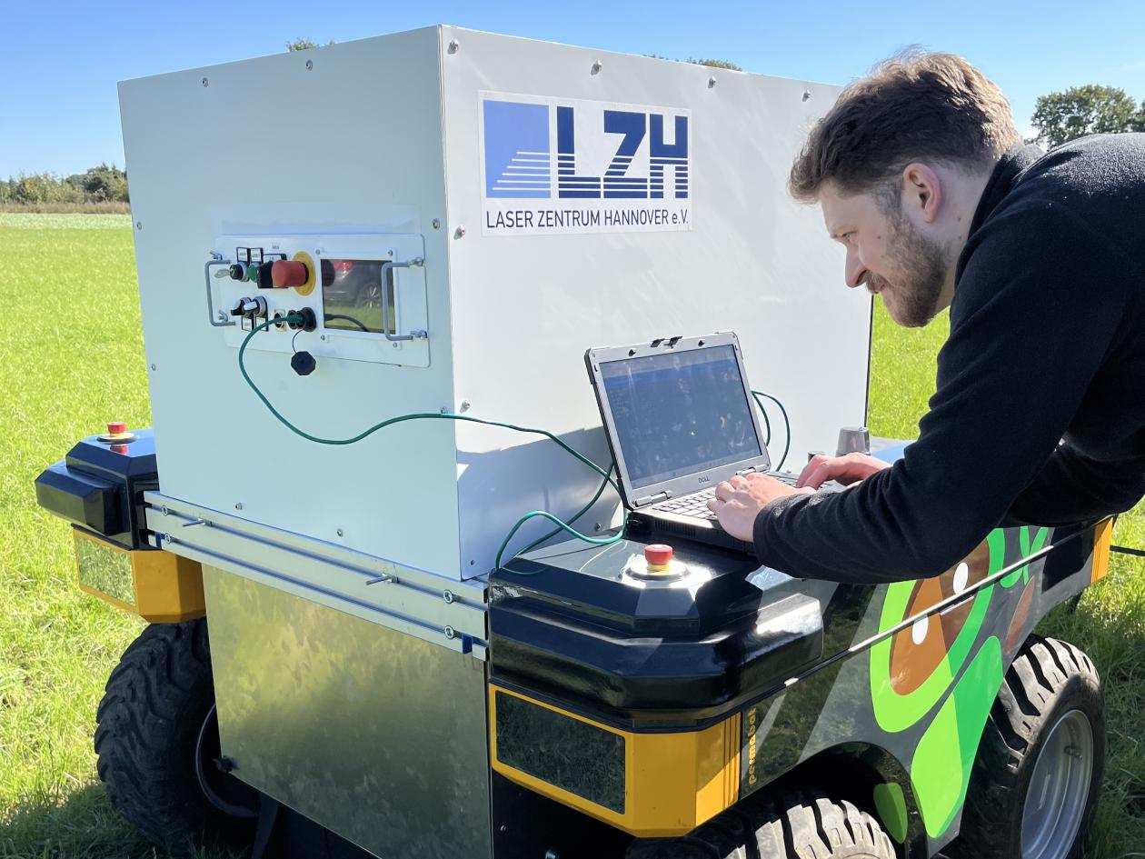 Wissenschaftler arbeitet mit Laptop an einem Feldroboter.