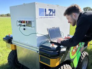 Wissenschaftler arbeitet mit Laptop an einem Feldroboter.