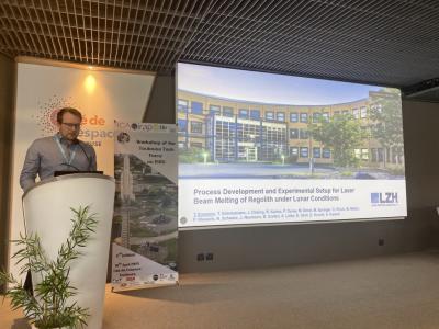 Mann hinter einem Pult neben einer Leinwand.