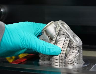 Hand mit Handschuh greift nach einem additiv gefertigten Bauteil.